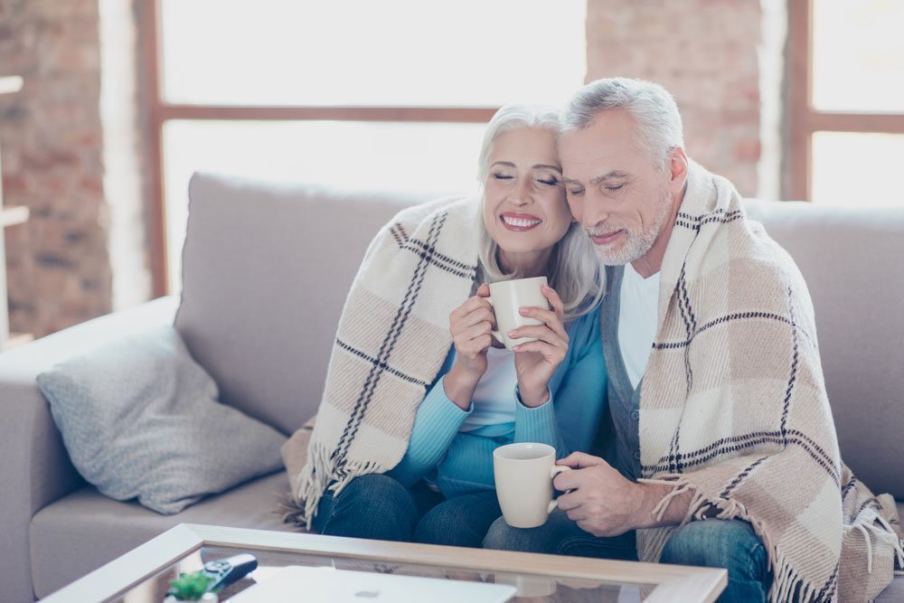 An elderly couple wrapped in a warm blanket enjoying a hot drink.