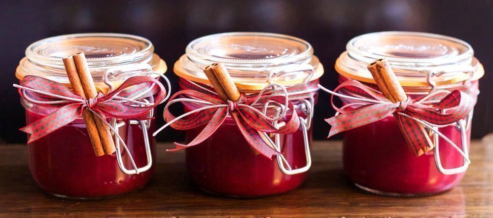 Homemade fruit jam presented in glass jars with a tartan bow and a stick of cinnamon.