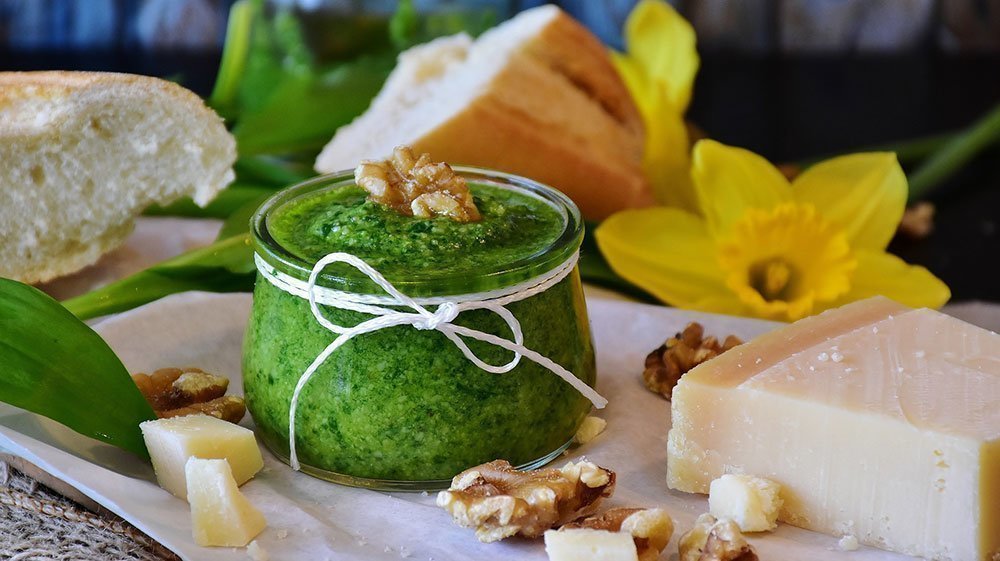Homemade green pesto in a glass ramekin, displayed with cheese, bread and nuts.