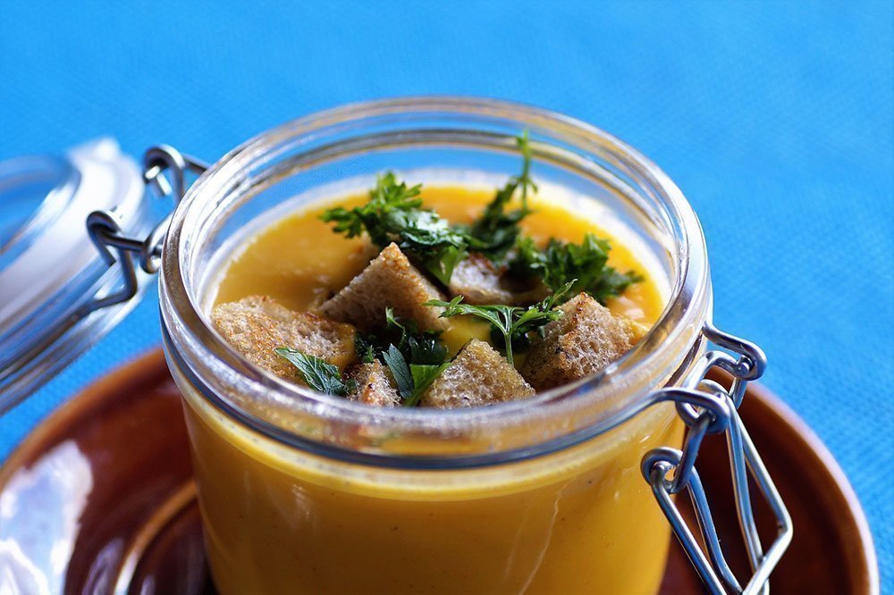 Homemade pumpkin soup topped with croutons and stored in a glass container.