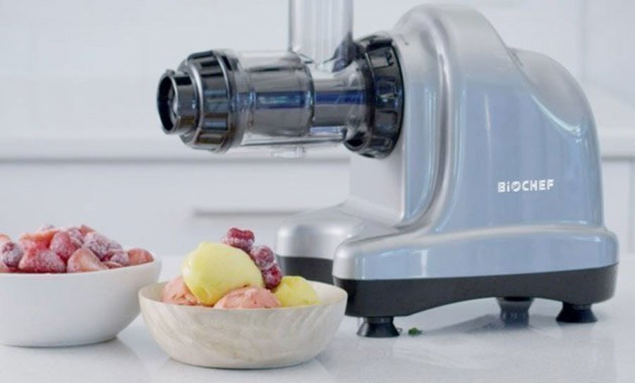 Horizontal BioChef Juicer on the kitchen countertop beside a couple of bowls of frozen fruit.