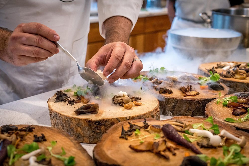 Professional chef plating up different types of mushrooms on a plate made of tree bark.
