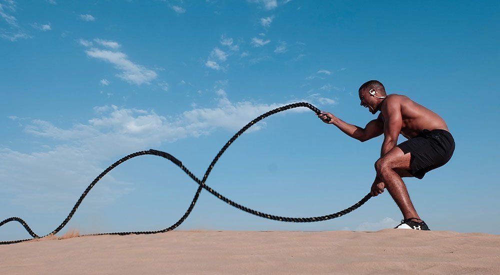Young man training outdoors with a rope, wearing wireless Bluetooth headphones.