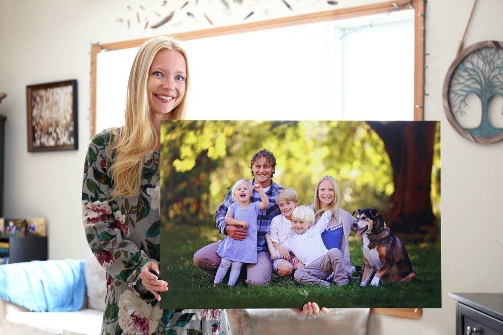 Young woman holding a canvas print of her family and their dog.